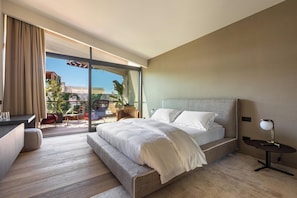 A modern hotel room with a large bed, a desk, and a balcony with outdoor seating.