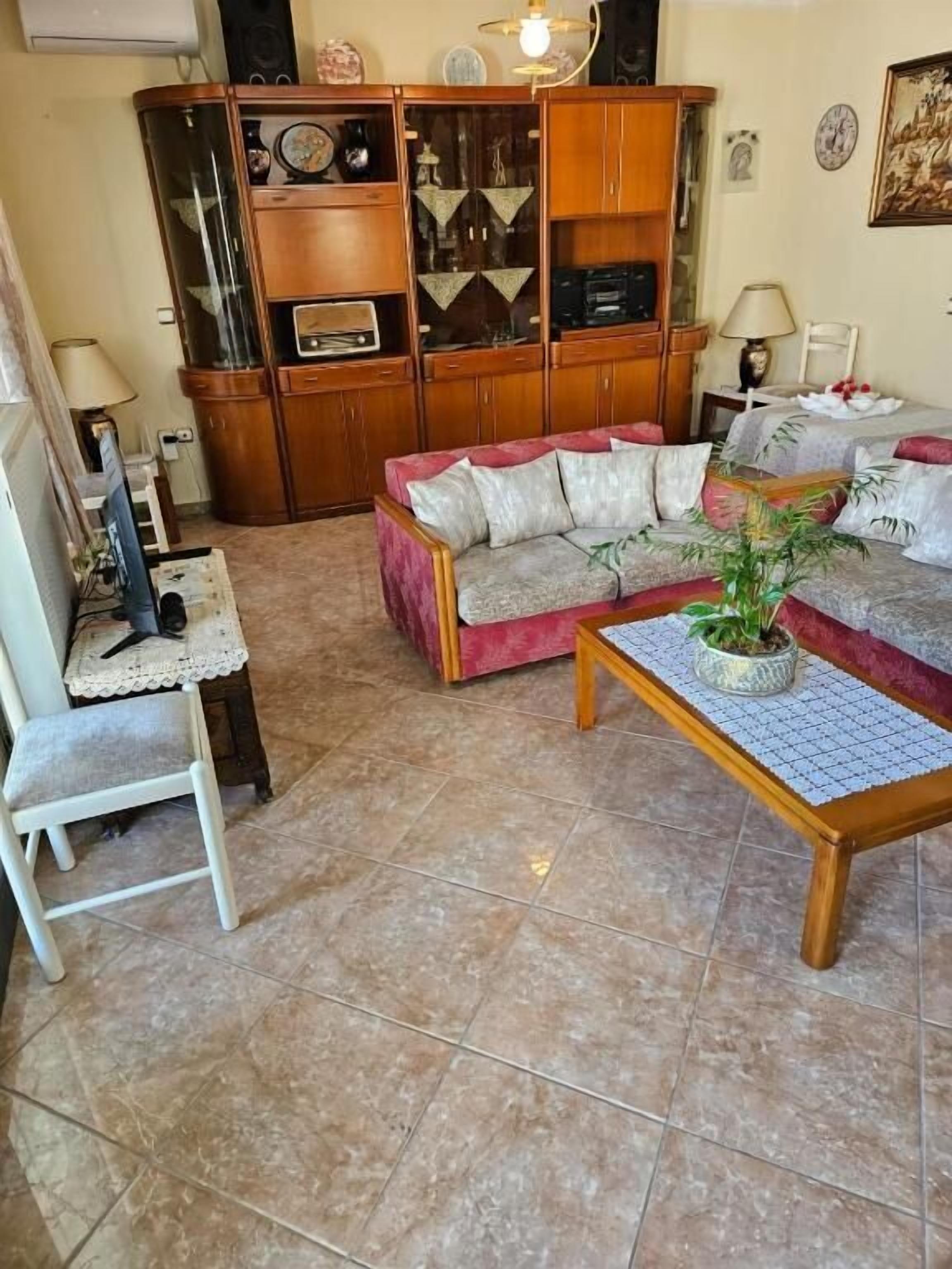 A living room with a sofa, a chair, a coffee table with a plant, a cabinet with various items, and a lamp.