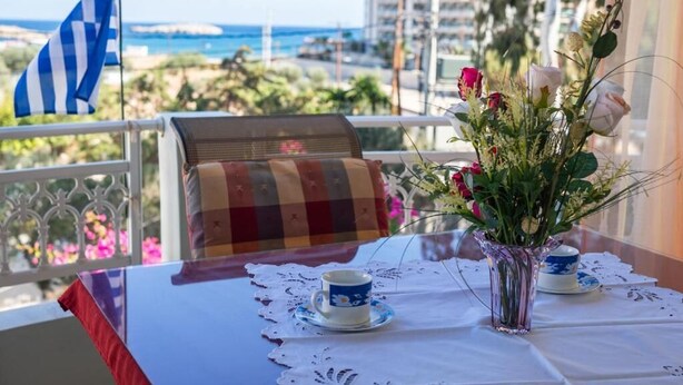 Un balcone con vista sul mare, un tavolo con una tazza e un vaso di fiori, e una bandiera.