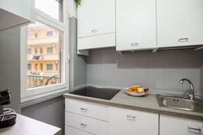 Cocina con armarios blancos, encimera negra, lavabo y ventana con vista a un edificio.