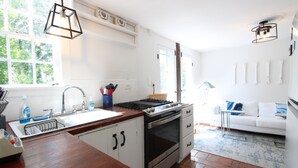 Et moderne køkken med komfur, vask og træbordplade. Der er en hvid sofa og en lampe i det tilstødende opholdsområde.