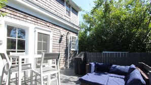 En patio med hvidt bord og stole, et overdækket grillområde og en blå sofa.