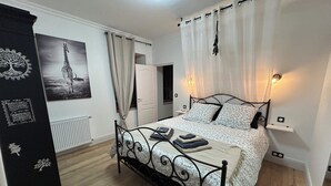 Um quarto com cama, guarda-roupa, radiador, porta e uma parede com um quadro emoldurado.