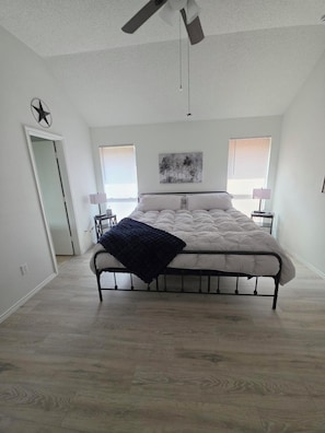 A bedroom with a bed, a ceiling fan, a star decoration, a painting, and two bedside lamps.