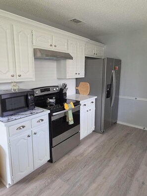 A kitchen with white cabinets, a stainless steel refrigerator, a microwave, and a stove.