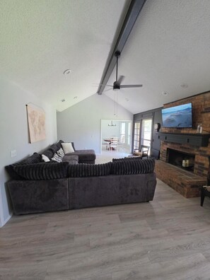 A modern living room with a sectional sofa, a fireplace, and a television mounted on the wall. - Christie Drive Retreat - Fully updated 3-bed, 2/bath house w/garage parking! (Frisco)