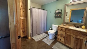 A bathroom with wooden cabinets, a toilet, a shower curtain, and a vanity with a mirror.