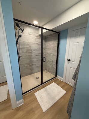 A walk-in shower with glass doors, a white door to the right, and a white rug on the floor. - Spacious Shawnee Home - Fenced Yard - Pets Welcome - Sleeps 8 (Shawnee)
