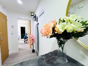 A hallway with a mirror, a vase of flowers, and a door labeled 'TOILET'.