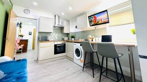 Eine moderne Küche mit Waschmaschine, einem Essbereich mit zwei Stühlen und einem an der Wand befestigten Fernseher.