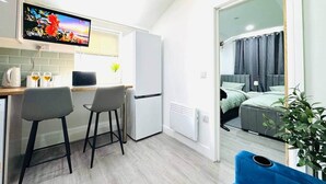 Eine kleine Küche mit Fernseher, zwei Barhocker, einem Kühlschrank und einem Essbereich.