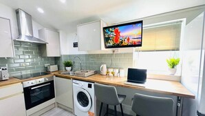 Eine moderne Küche mit eingebauter Waschmaschine, einem an der Wand montierten Fernseher und einem Fenster mit Jalousien.