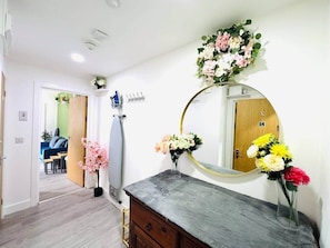 A room with a wooden door, a mirror with a gold frame, a dresser, and a vase with flowers. - Stylish 2-Bed Flat in Cardiff (Cardiff)