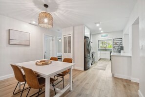 Eine moderne Küche mit weißen Schränken, einem Edelstahl-Kühlschrank und einem Essbereich mit weißem Tisch und braunen Stühlen.