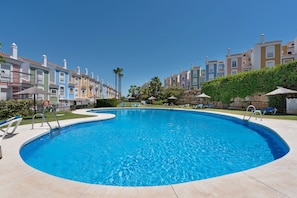 A swimming pool surrounded by colorful buildings, a clear sky, and lounge chairs.