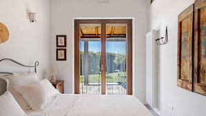 Ein Schlafzimmer mit Bett, Nachttisch, Wandlampe und einem großen Fenster mit Blick auf Grünflächen.