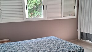 A bedroom with a bed, a window with blinds, a curtain, and a wall-mounted air conditioning unit. - Prainha, Rio de Janeiro (Rio de Janeiro)
