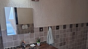 A bathroom with a wooden vanity, a sink with a decorative basin, a mirror, and a towel hanging on the wall. - Prainha, Rio de Janeiro (Rio de Janeiro)