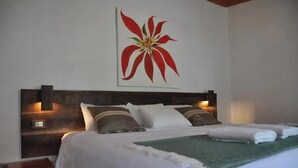 Una cama con ropa de cama blanca, un plaid verde y un cuadro de una flor roja en la pared.
