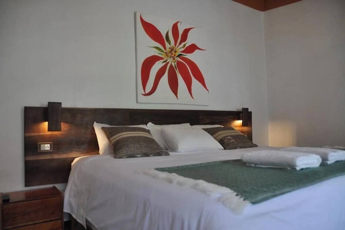 Un letto con biancheria bianca, una coperta verde e un quadro con un fiore rosso appeso al muro.