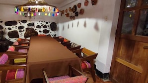 Un comedor con una mesa larga, sillas, una lámpara decorativa colgante y una pared con estampado de vaca.