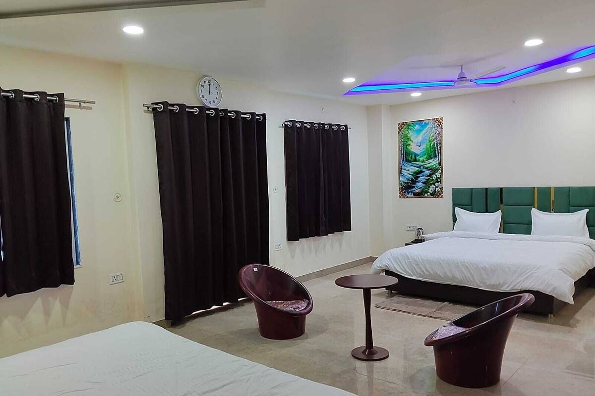 A hotel room with two beds, a small table, two chairs, a painting on the wall, and a ceiling light.