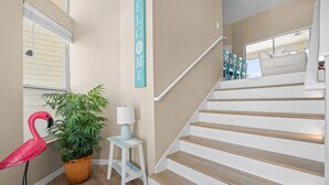 Eine Treppe mit hölzernen Stufen und einem weißen Geländer, ein Blumentopf, ein kleiner weißer Tisch mit einer Lampe und eine Flamingo-Dekoration.