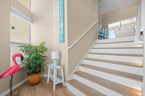 A staircase with wooden steps and a white railing, a potted plant, a small white table with a lamp, and a flamingo decoration. - The Oasis (Fort Myers Beach)
