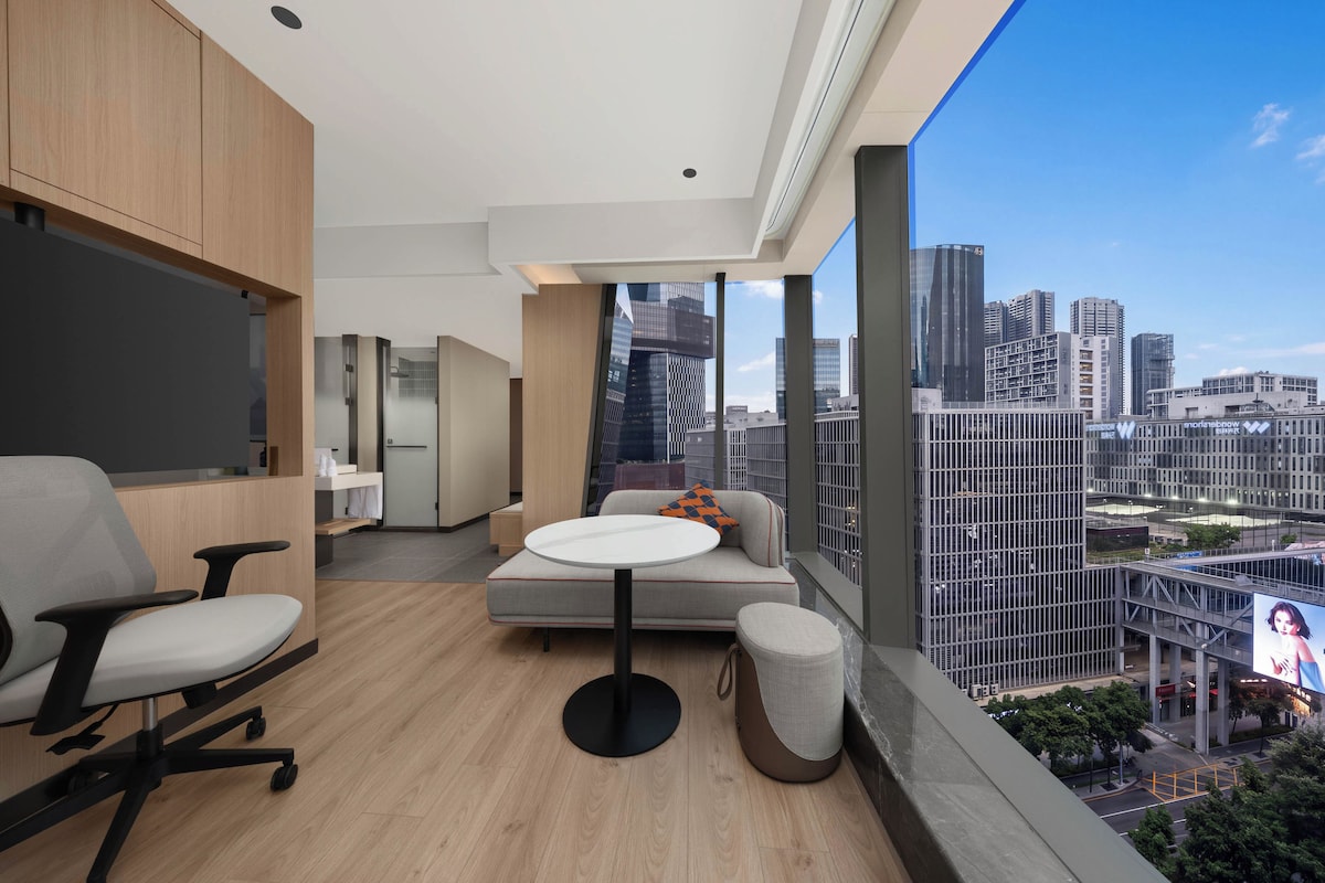 Una habitación de hotel moderna con vistas a la ciudad, una mesa redonda, un sofá y un escritorio.