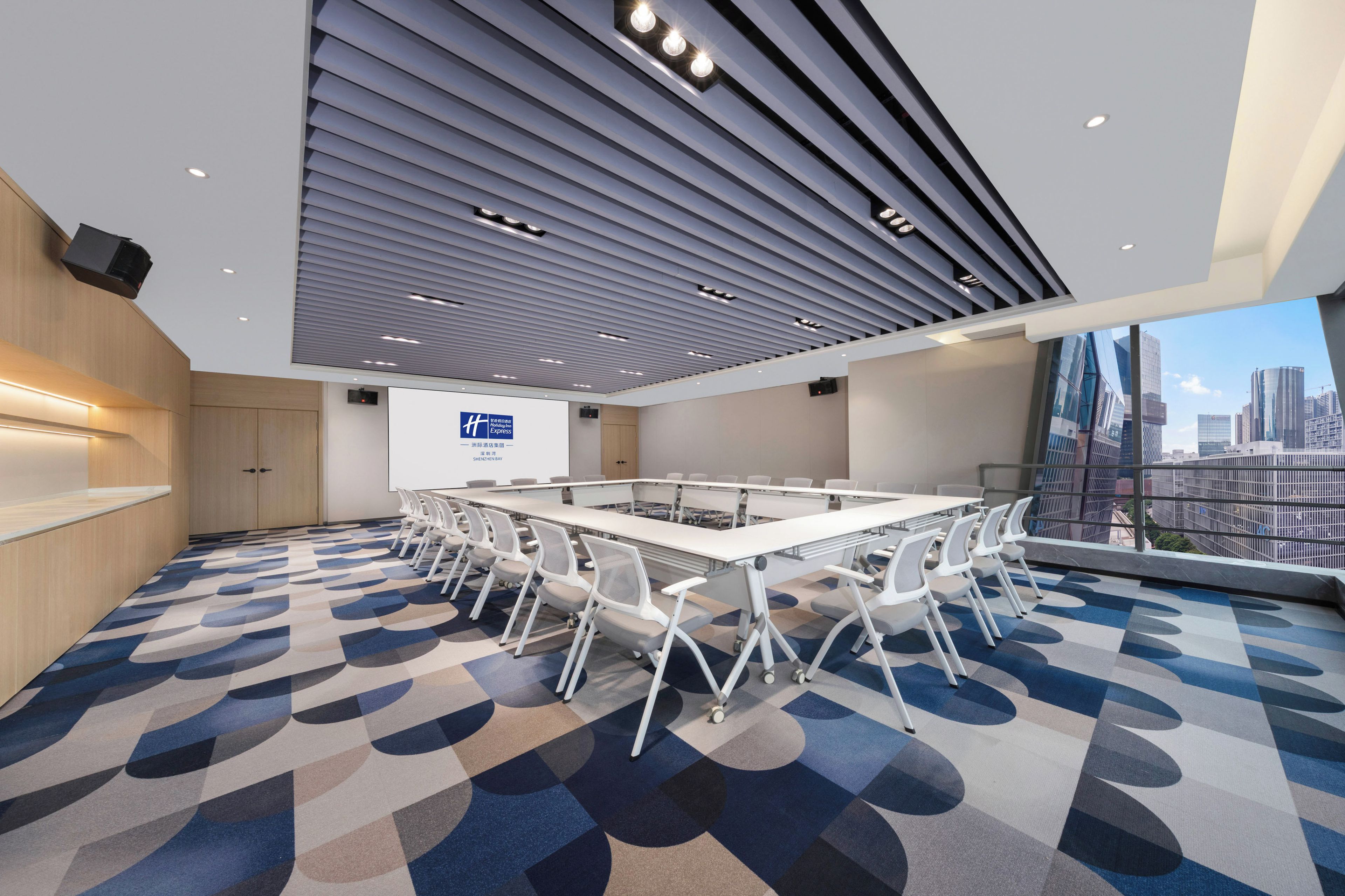 Een moderne vergaderzaal met een grote tafel, stoelen, een presentatiescherm en uitzicht op de stad door grote ramen.