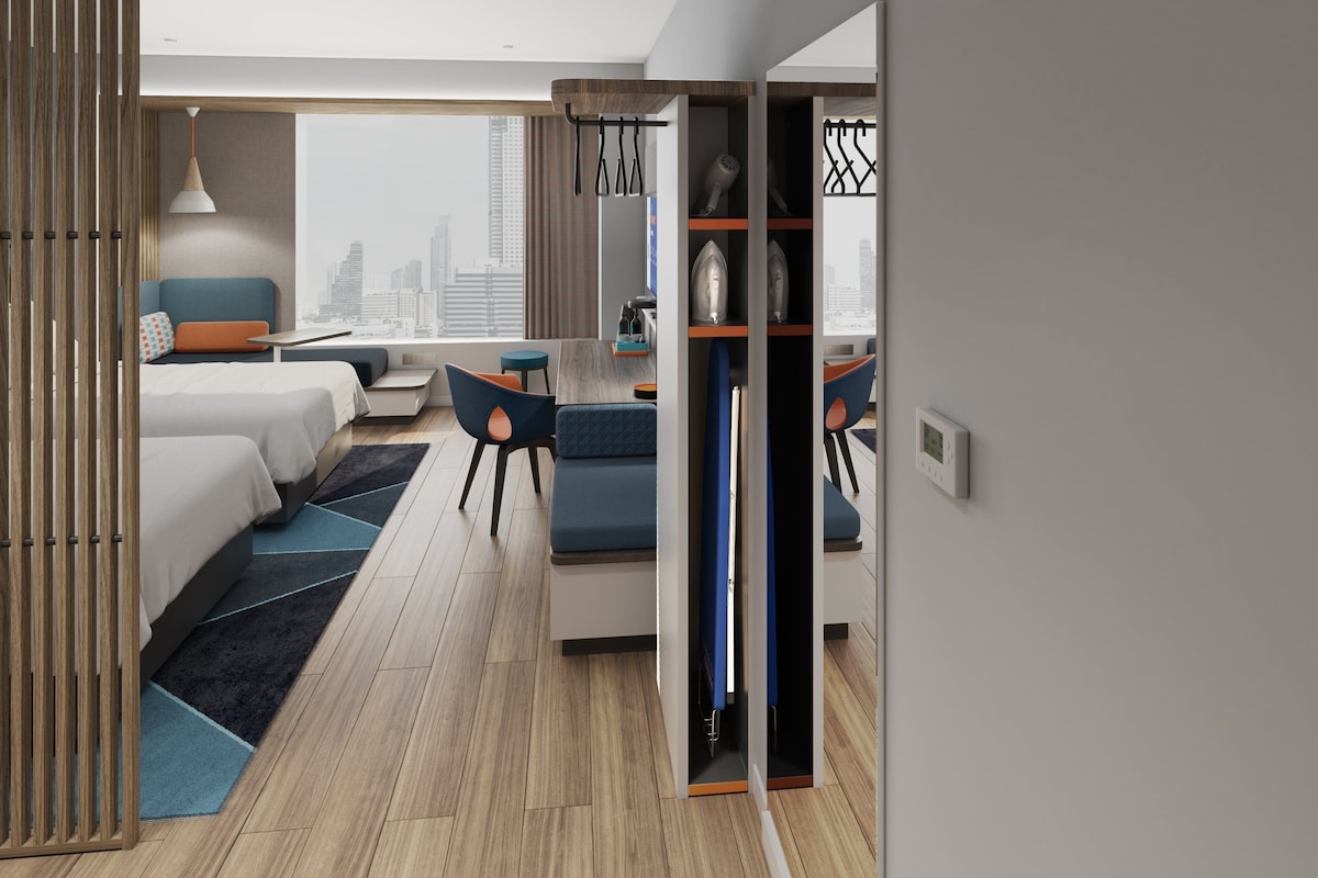 A modern hotel room with a bed, seating area, and a view of the city.