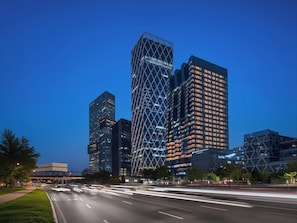 Un paisaje urbano con modernos rascacielos y una avenida con varias pistas iluminadas por las luces de los vehículos en movimiento.
