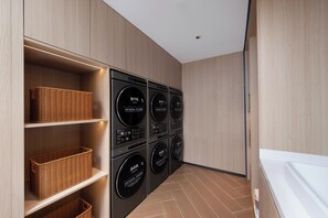 A laundry room with four stacked washing machines and dryers, wooden shelving with baskets, and a tiled floor. - Holiday Inn Express Shenzhen Bay By Ihg (Shenzhen)