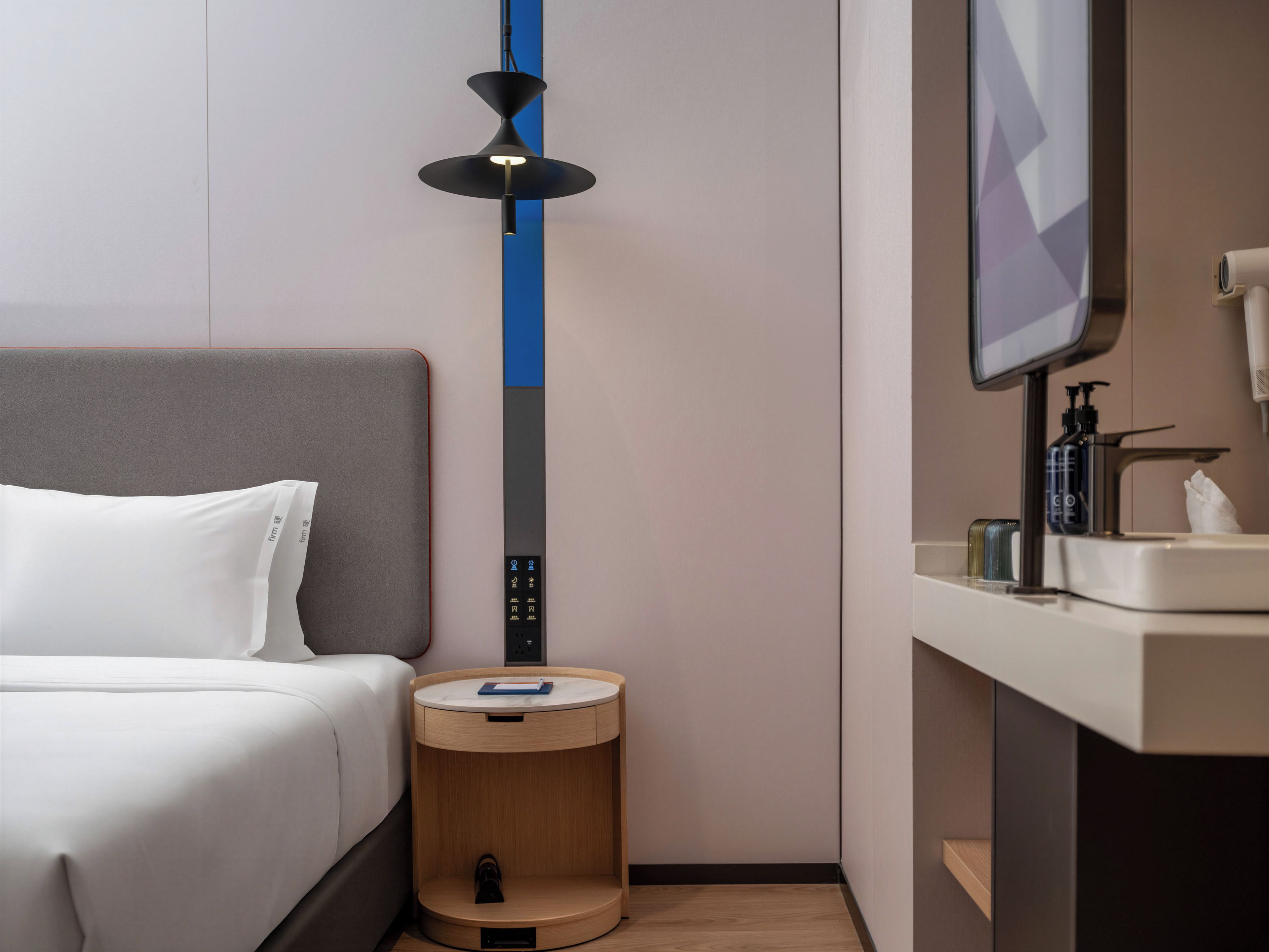 A hotel room with a bed, bedside table, and a wall-mounted TV.