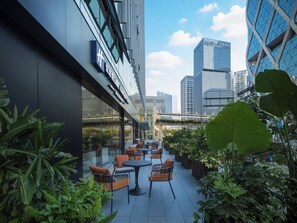 An outdoor seating area with wicker chairs and tables, surrounded by greenery, with a cityscape in the background. - Holiday Inn Express Shenzhen Bay By Ihg (Shenzhen)