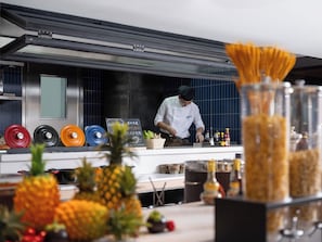Un cocinero preparando comida en una cocina con mostrador de acero inoxidable, diferentes utensilios de cocina e ingredientes como piñas y botellas de salsas.