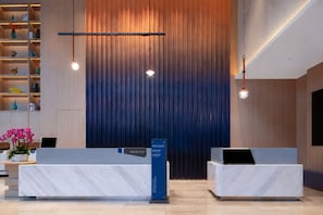 Zona de recepción con diseño moderno, que incluye dos mostradores, un panel de madera vertical y un atril informativo azul.