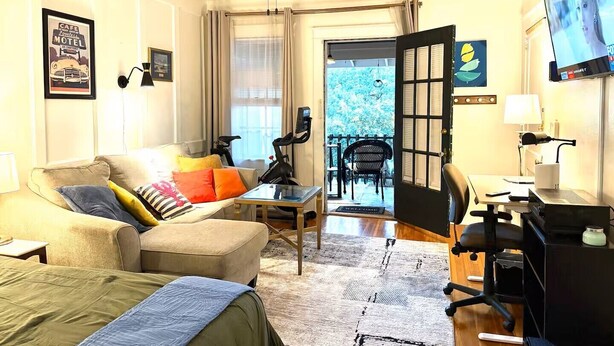 A living room with a sofa, a coffee table, a desk with a chair, a ceiling fan, and a TV. - Cozy Vintage Studio Close To Downtown (Mobile)