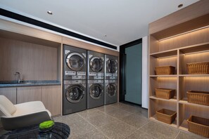A laundry room with four washing machines, a sink, a chair, and shelves with baskets. - Holiday Inn Express Huangshan Tunxi High-Tech Zone By Ihg (Huangshan)