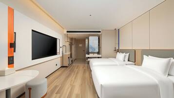 Habitación de hotel moderna con una gran televisión de pantalla plana, un escritorio, un otoman redondo, dos camas y vistas a la ciudad.