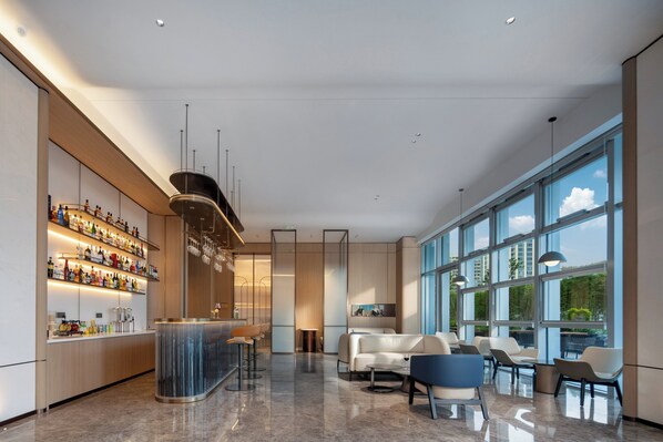 A modern bar area with a curved counter, seating with a mix of chairs and sofas, and large windows offering a view of the sky and buildings. - Holiday Inn Express Huangshan Tunxi High-Tech Zone By Ihg (Huangshan)