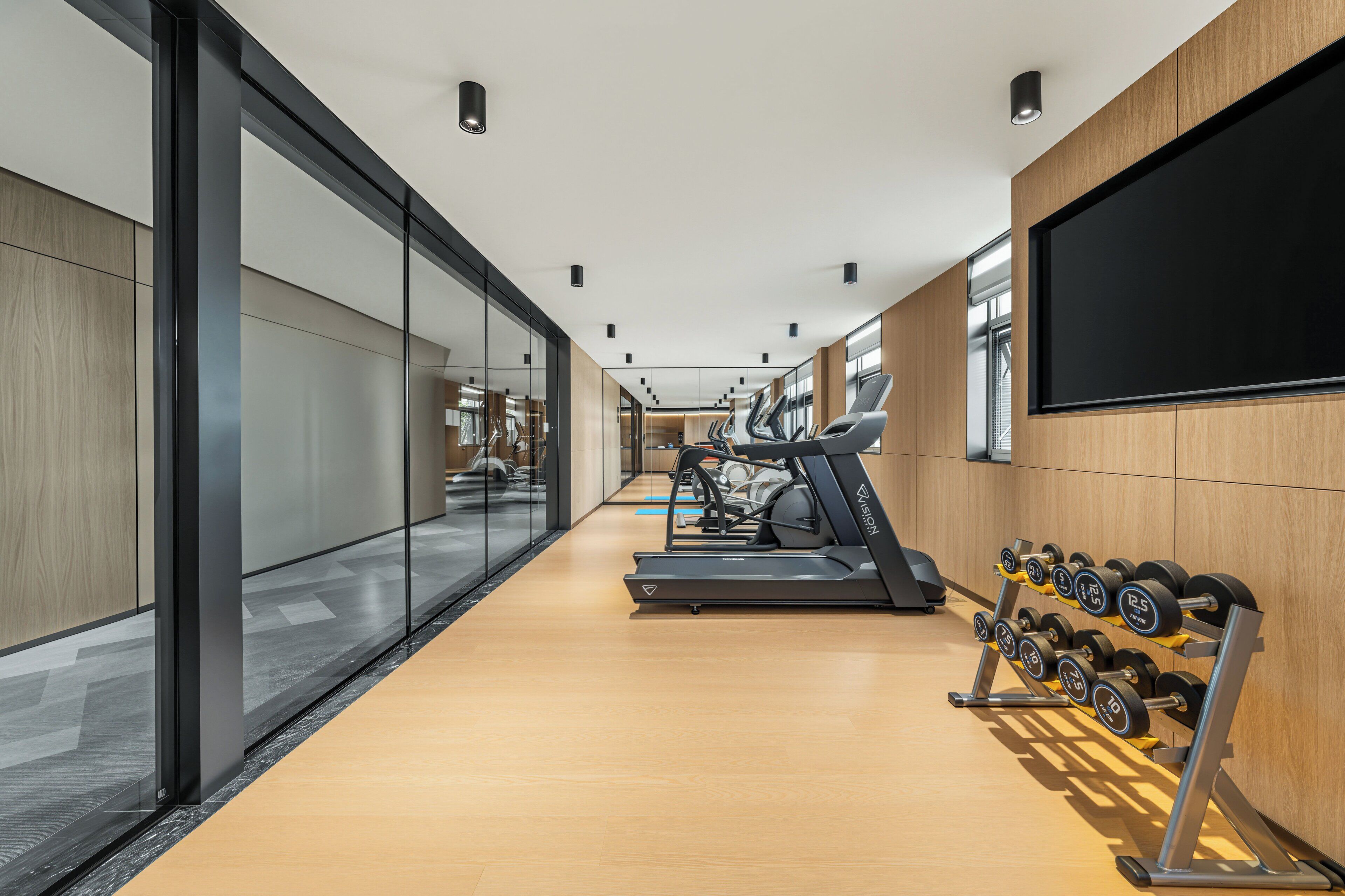 A modern gym with exercise equipment, a wall-mounted TV, and a wooden floor.