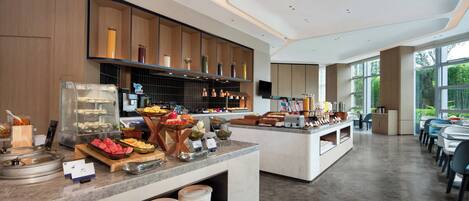 A modern breakfast buffet with various food items, a glass display case, and a seating area with tables and chairs.