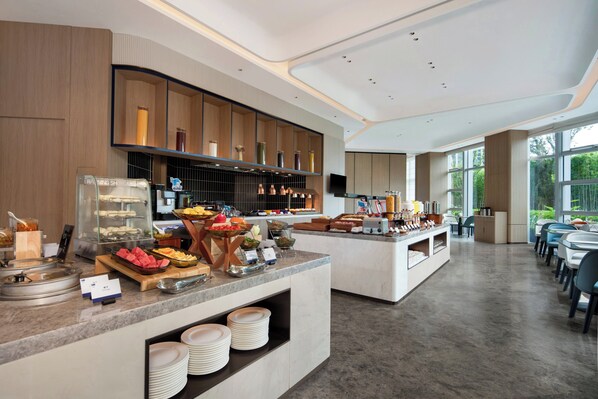 A modern breakfast buffet with various food items, a glass display case, and a seating area with tables and chairs. - Holiday Inn Express Huangshan Tunxi High-Tech Zone By Ihg (Huangshan)