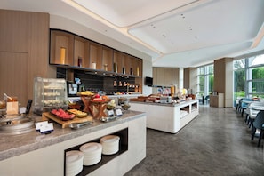 En moderne morgenmadsbuffet med et udvalg af mad, et glasdisplay og et siddeområde med borde og stole.