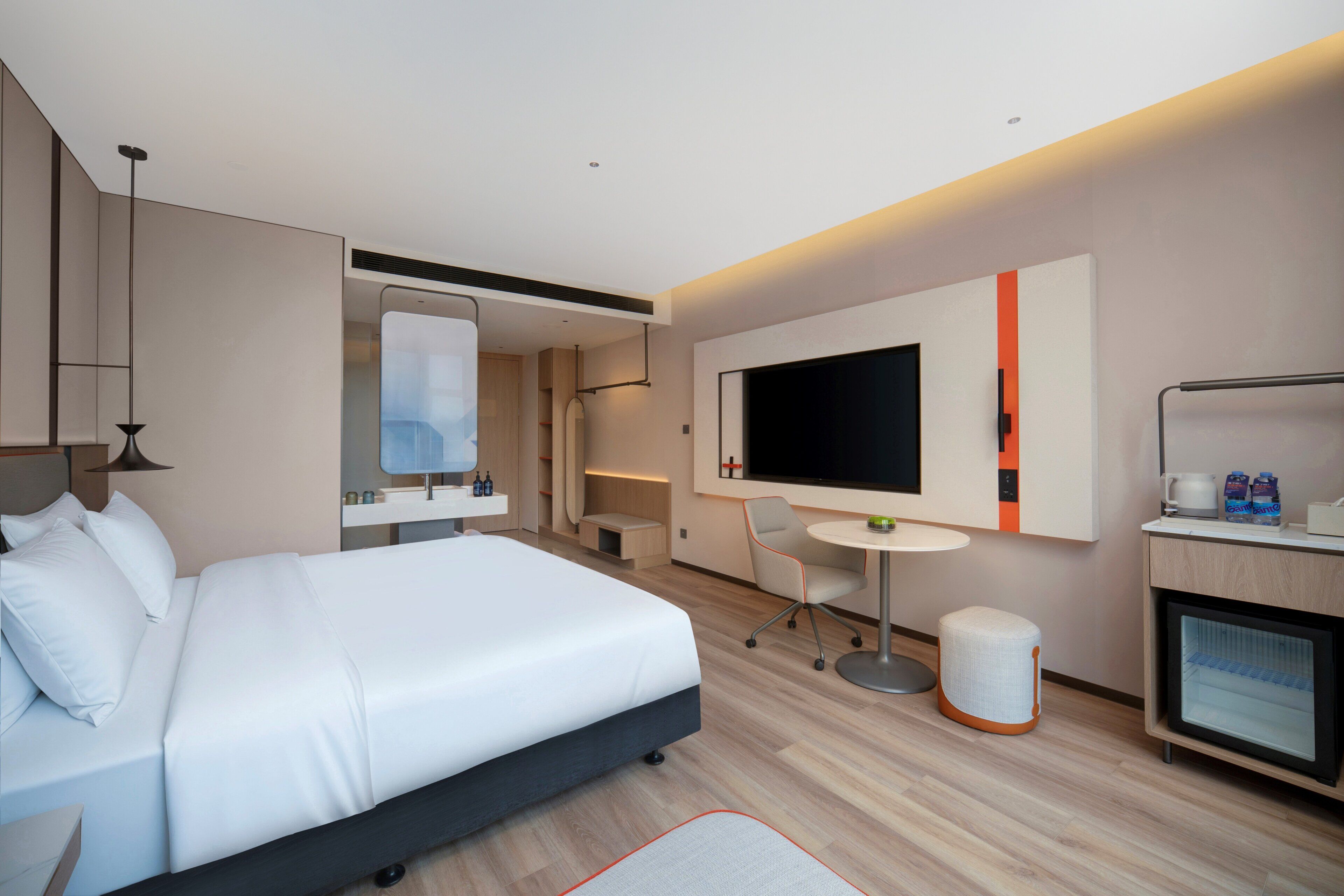 Moderni hotellihuone, jossa on suuri sänky, televisio, pieni pöytä, tuoli ja minibaari.