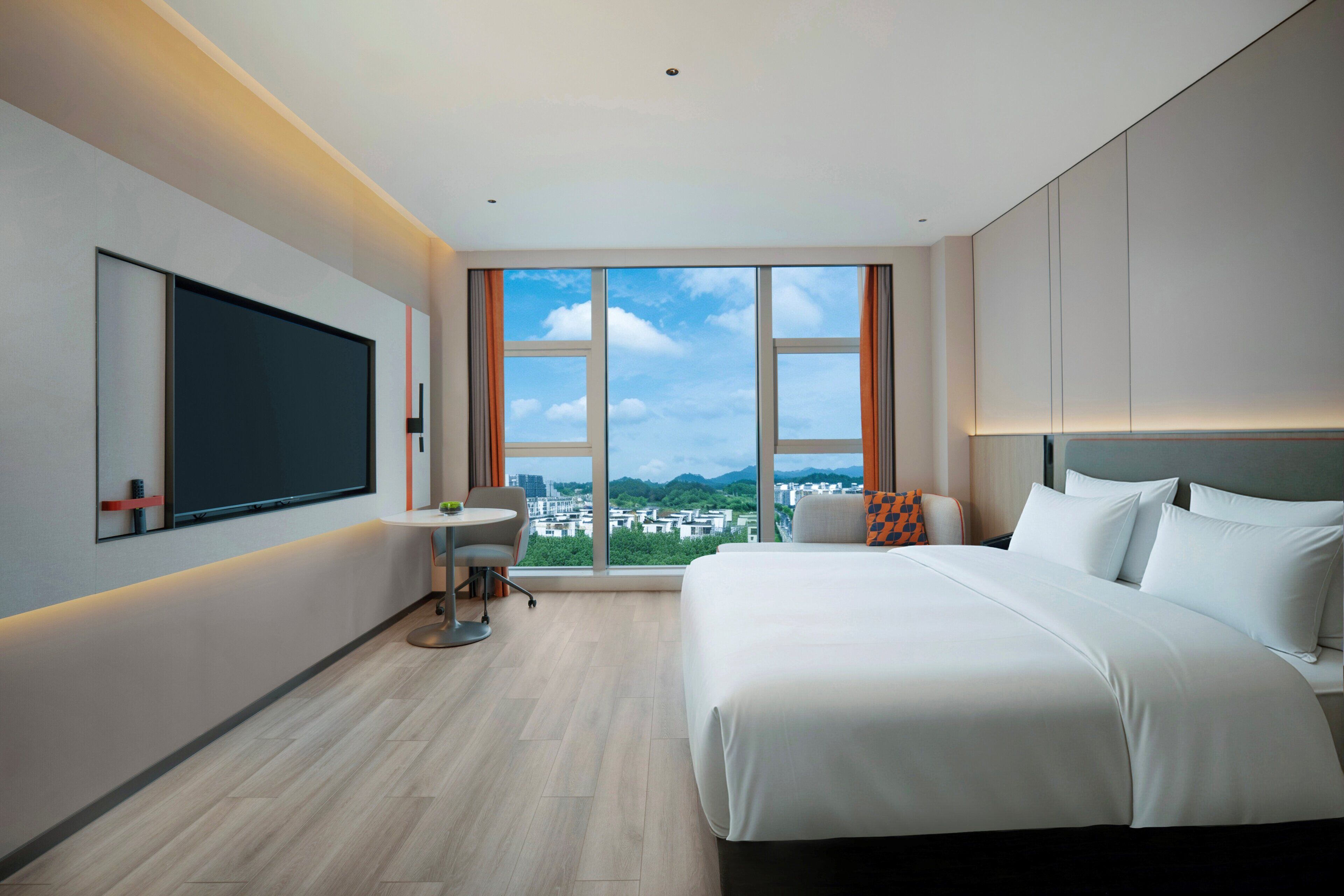 A modern hotel room with a large bed, a desk, a chair, and a large window offering a city view.