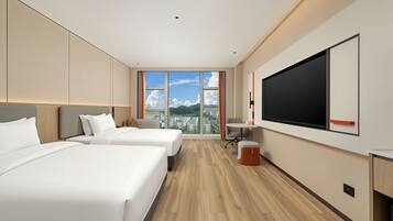 Habitación de hotel moderna con dos camas, un televisor grande y vista a la ciudad.