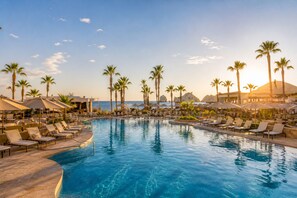 Ein Pool in einem Resort mit Liegestühlen, Palmen und Blick auf den Ozean.