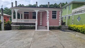 Une maison à deux étages avec un porche, une cheminée et un bâtiment vert attenant.